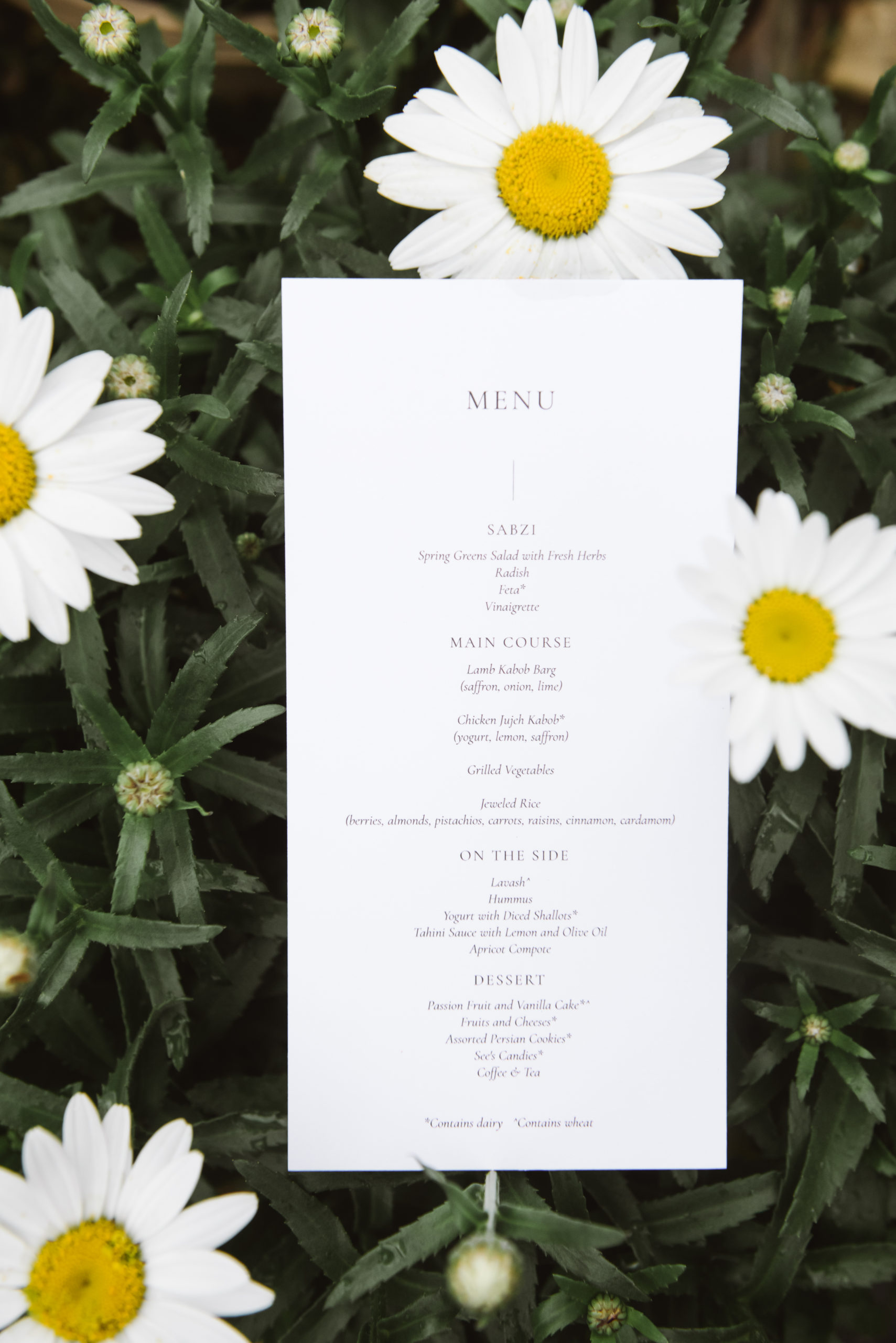Detail of the wedding menu set atop greenery and white petal flowers.