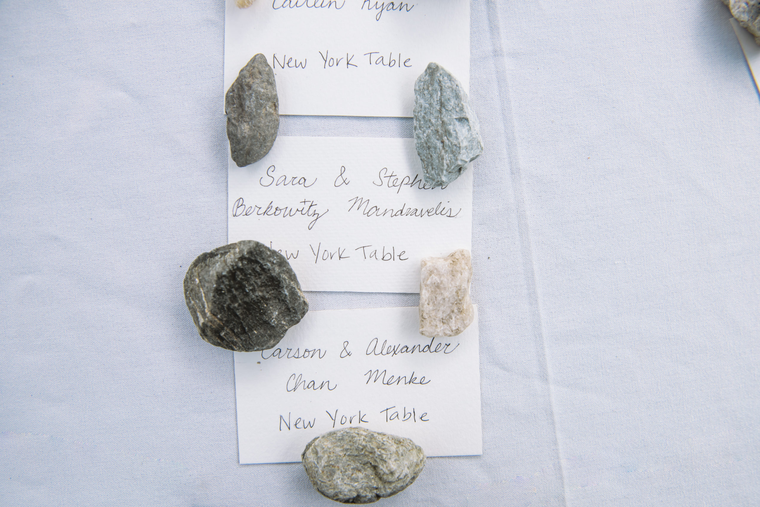 Hand written escort cards featuring natural stones as paperweights on a white table cloth.