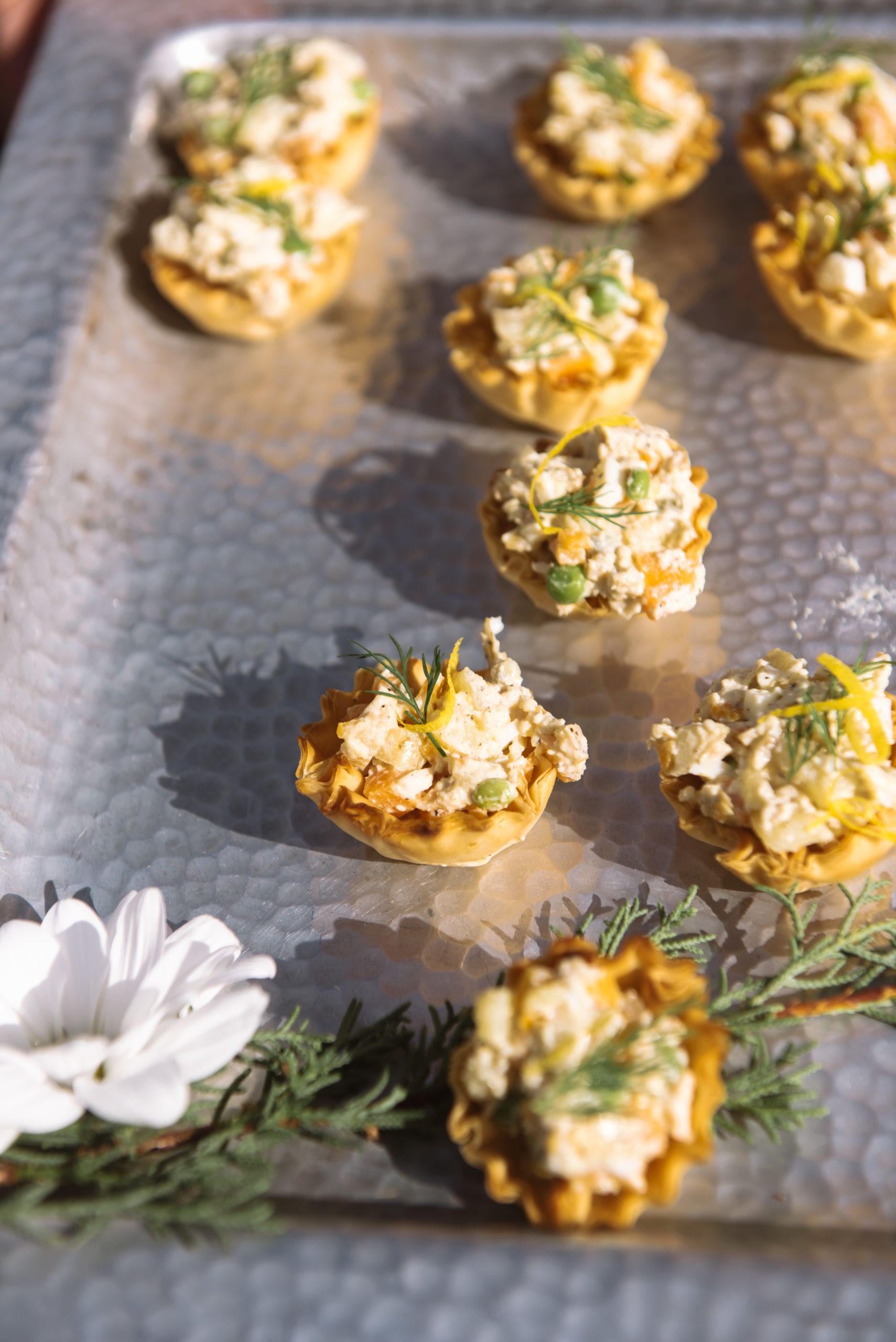 Close up of some hors d'oeuvres served during cocktail hour on a silver platter. They are mini crusts filled with a spread and herbs.