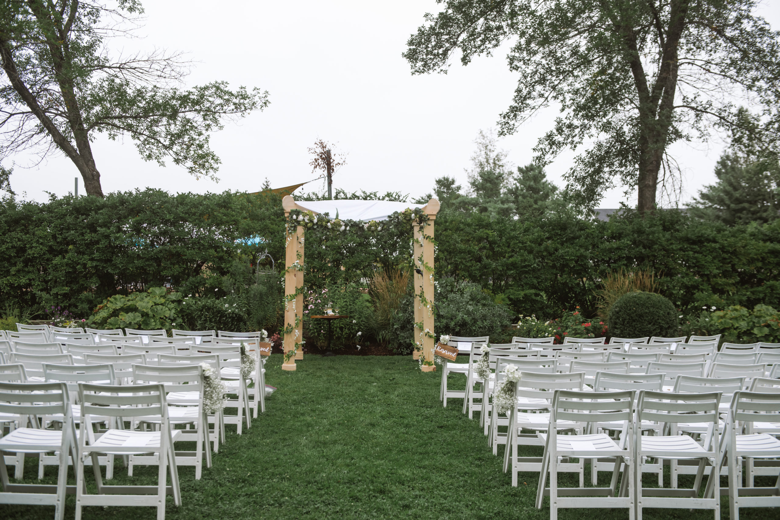 Empty ceremony space featuring the light-wood chuppah which is adored with greenery and white florals.