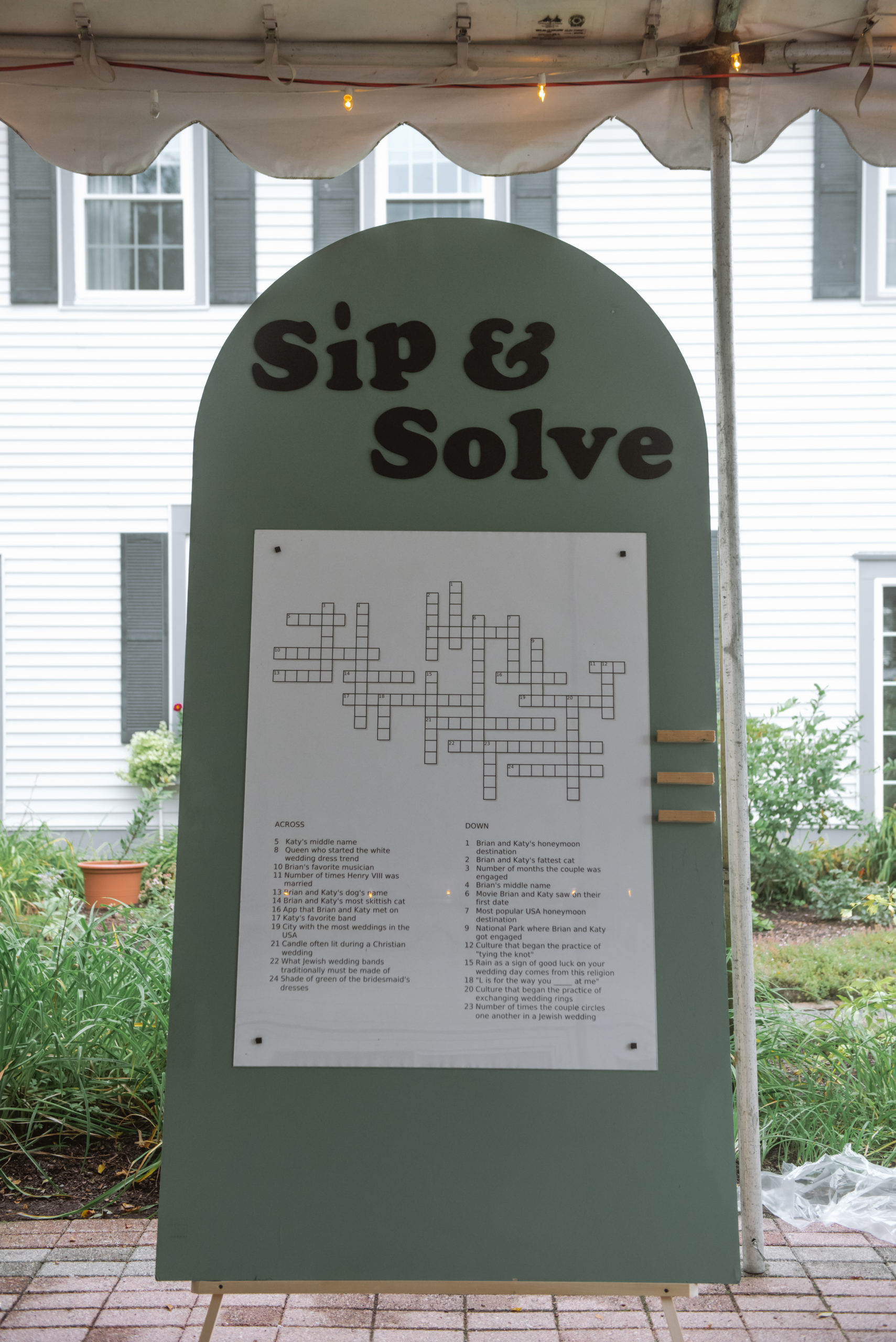 "Sip & Solve" written on a wooden arch-shaped board with a huge crossword puzzle full of the couple's details/trivia about them for cocktail hour guests to solve.