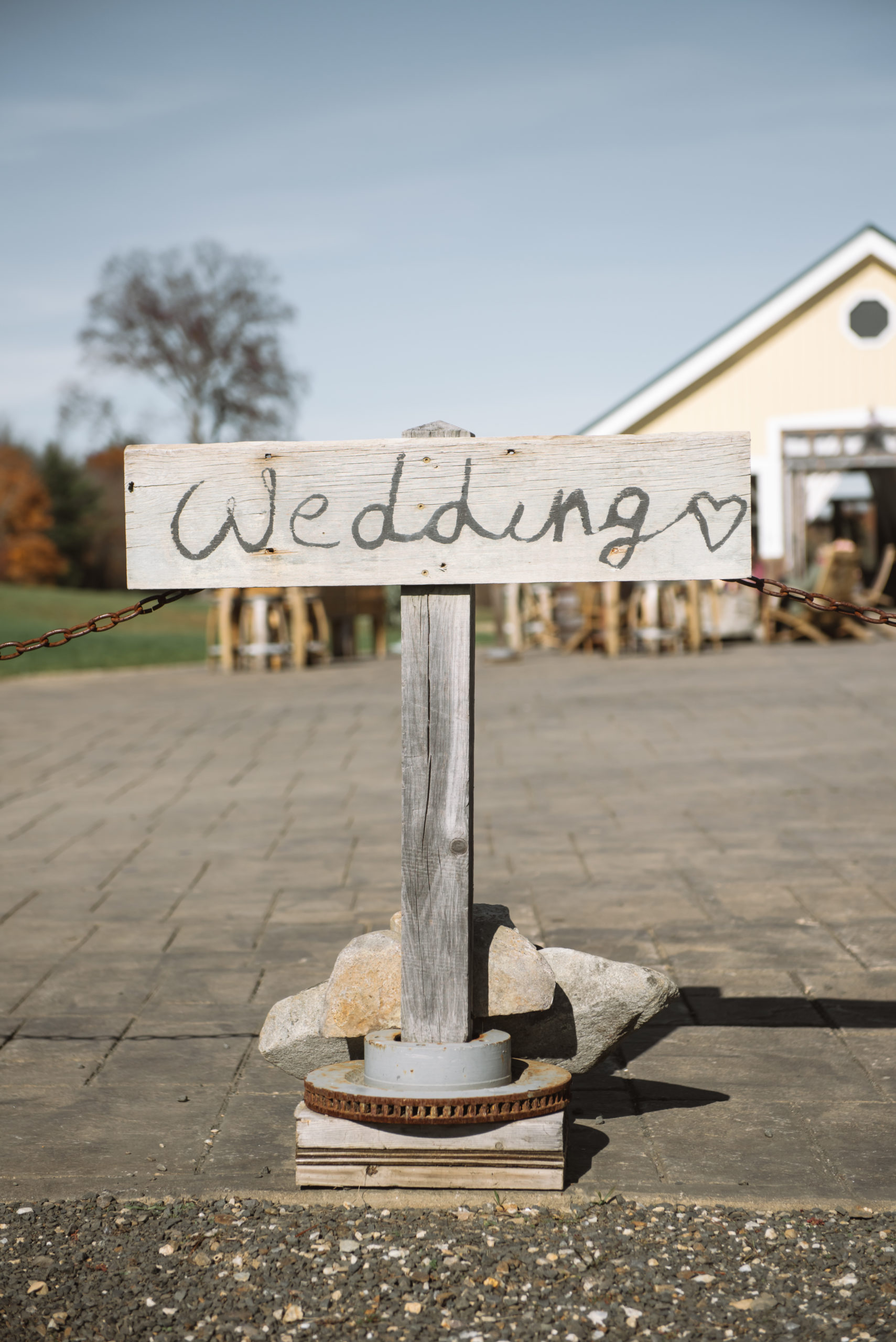 Detail of the "Wedding [illustrated hear]" wooden sign placed at the entrance of the ceremony/reception courtyard area. The ceremony location is partially visible in the background.