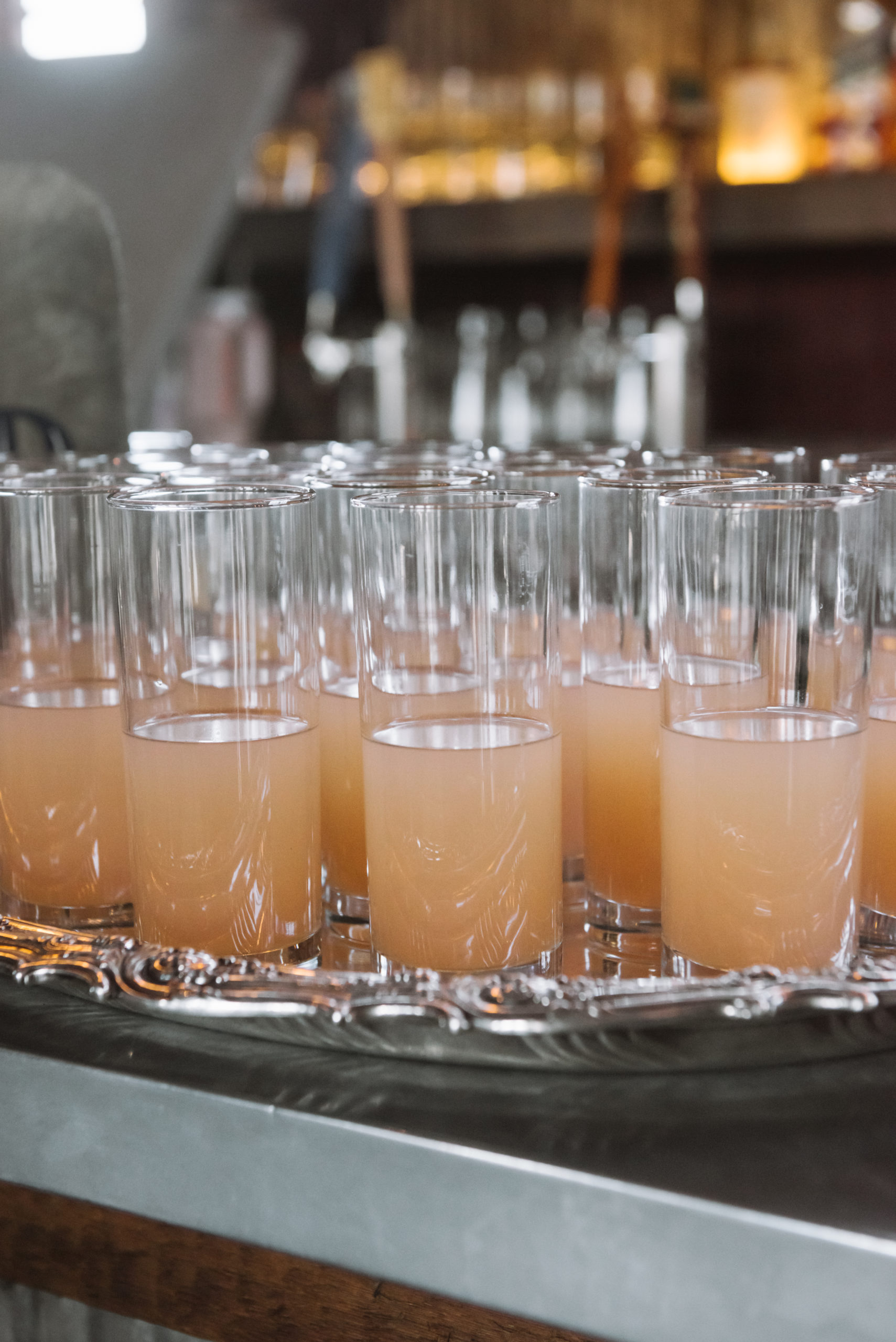 Detail of the pink-orange signature cocktail "Torre de Palma". There are multiple of them set atop a silver tray on the bar counter.