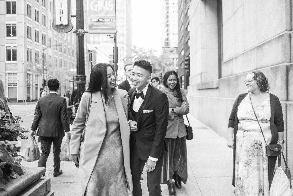 Black and white photo of wedding party walking along a Chicago sidewalk next to City Hall.
