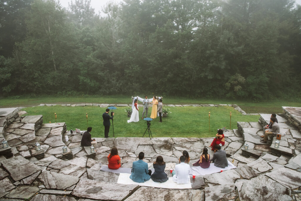 A wide-shot of a wedding ceremony with 11 guests sitting spaced out on stone.