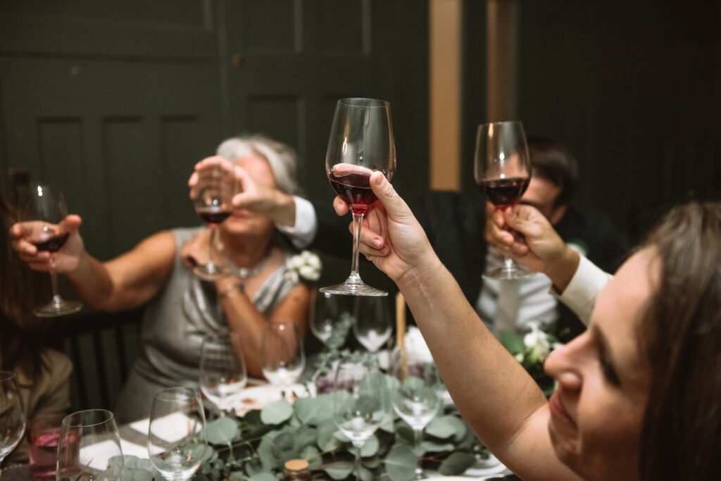 A table of wedding guests toasts with glasses of red wine. 