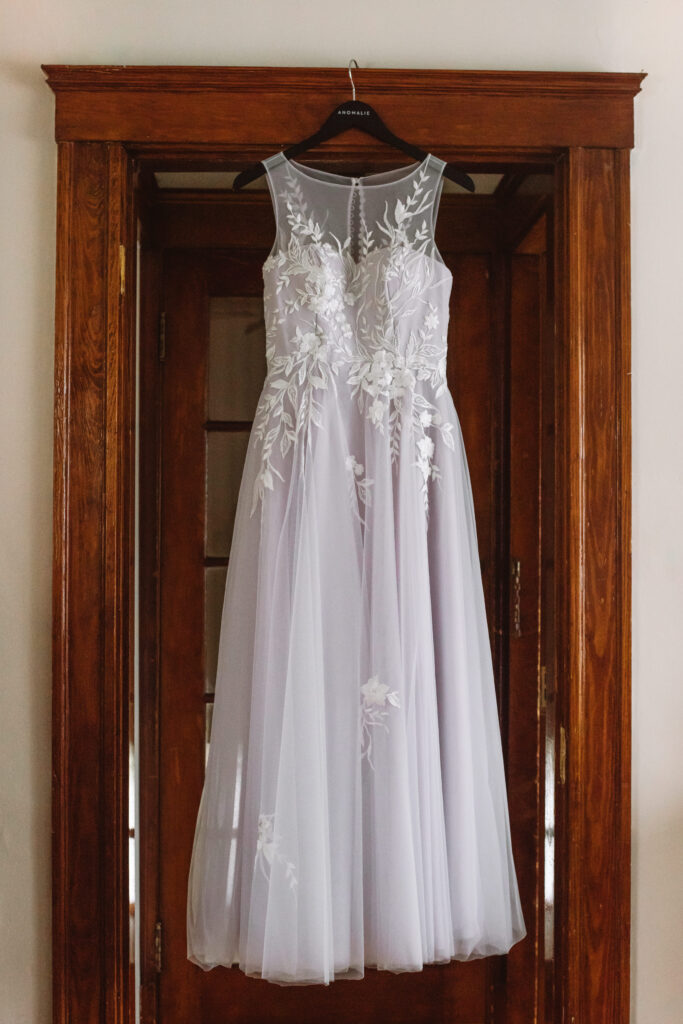 A sleeveless ankle length wedding dress  hangs in a wooden doorframe. 