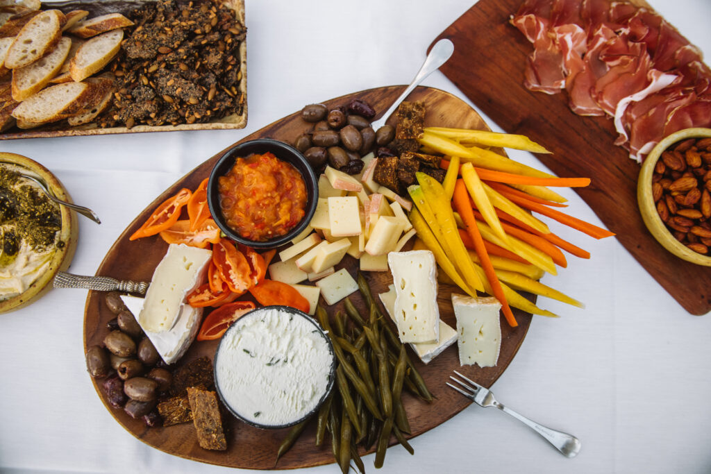 Overhead view of various boards featuring charcuterie, cheese, vegetables, and more.