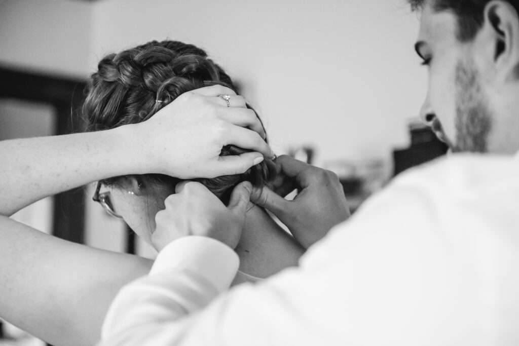 One person adjusts the necklace clasp of another. 