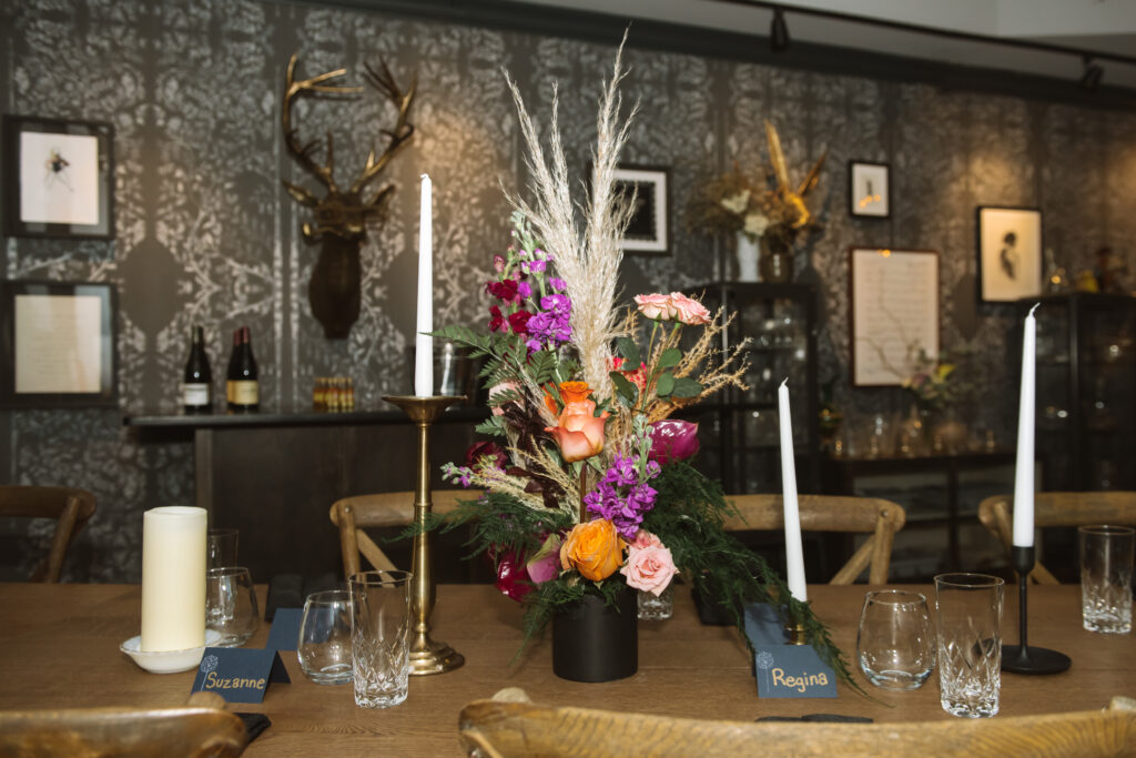 A table with a colorful floral centerpiece and white tapered candles. 